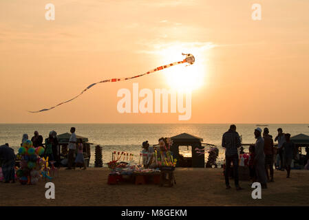 Local people and stall holders with a kite in the air on Galle Face Green at sunset - a popular spot in Colombo to spend time playing by the sea. Stock Photo