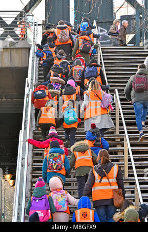 Group of primary school children on school trip in high vis jacket or vest with teacher & assistants climbing steep steps onto footbridge London UK Stock Photo