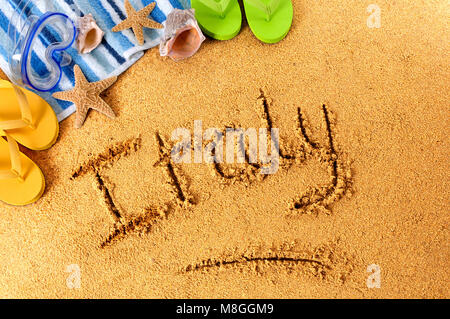 The word Italy written on a sandy beach, with scuba mask, starfish and flip flops. Stock Photo