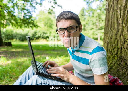 Dissatisfied guy at work on laptop sitting under tree Stock Photo