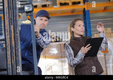 forklift driver talking with his manager in a large warehouse Stock Photo