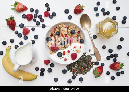 Breakfast bowl of granola, fruit, seeds, yogurt and honey on a white wood background Stock Photo