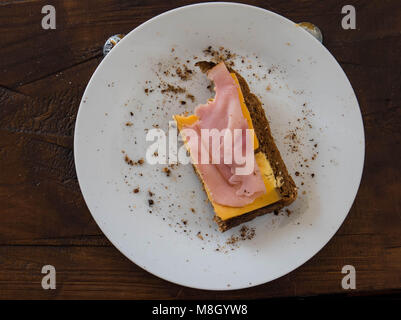 Rye bread with ham and cheese missing a bite on a white plate on a wooden table image with copy space Stock Photo