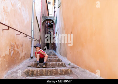 Young boy in red Tshirt, a hat and sun glasses having fun on stairs in a tiny street of Provencal village of Roussillon, France Stock Photo