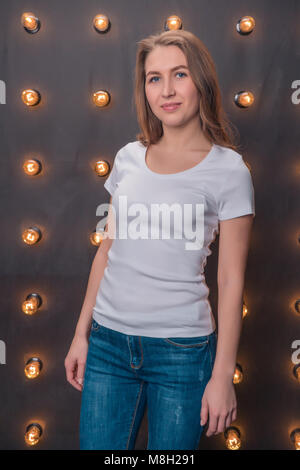 Beautiful girl in classic white t-shirt and jeans against a background of lights Stock Photo