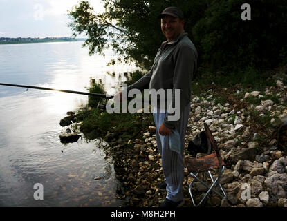 side view fisherman in a gray dress with a fishing rod in hand Stock Photo