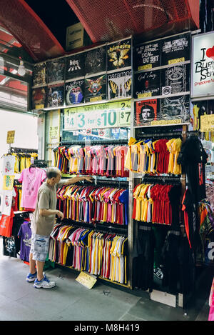 Bugis Street, Singapore. A shop keeper or assistant arranges his wall of flashy affordable t-shirts for sale at this budget shopping venue. Stock Photo
