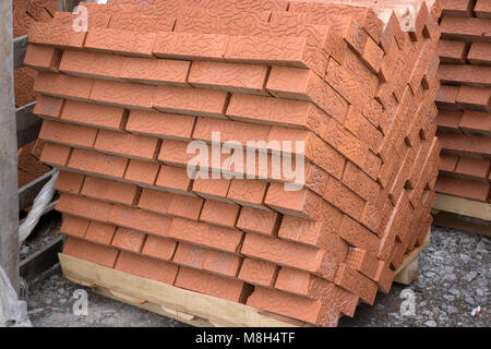 Red clay building bricks stacked on pallets still wrapped in their plastic for delivery at a warehouse, factory or construction site. Stock Photo