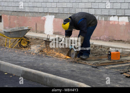 Close up of trained worker in protective workwear, gloves and glasses using angle grinder to smooth metal of profile pipe in workshop. Concentrated on Stock Photo