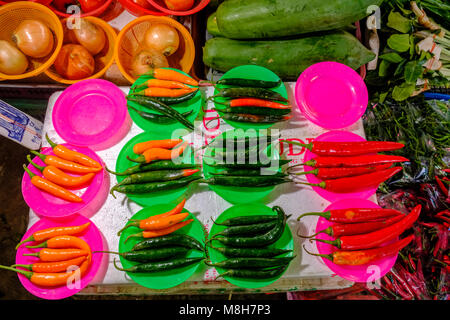 Fresh chillis, arranged on colorful plastic plates, are for sale at Nonthaburi Market Stock Photo
