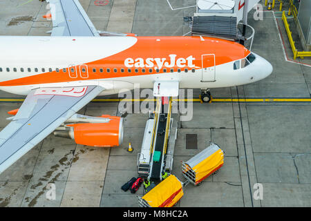High perspective of baggage handlers picking up suitcases from a conveyor belt connected to an Airbus A320 easyJet airplane at London Gatwick's North Terminal