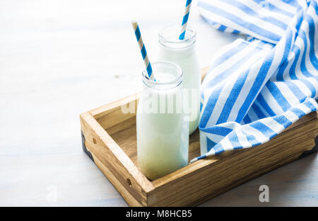 Milk in vintage bottles with stripped blue and white straws in wooden box on white rustic table with copyspace Stock Photo
