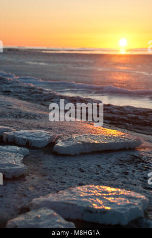 Sunrise and Bering Sea ice. As sea ice forms in the Bering Sea, it comes first as flat chunks for several weeks, floating in the salty, slushy, sluggish waves. Smaller shards sound like broken glass tinkling as they wash up on shore. Stock Photo