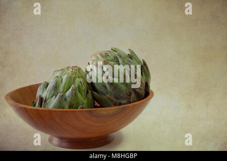 Two artichokes in wooden bowl with grunge background and copy space Stock Photo