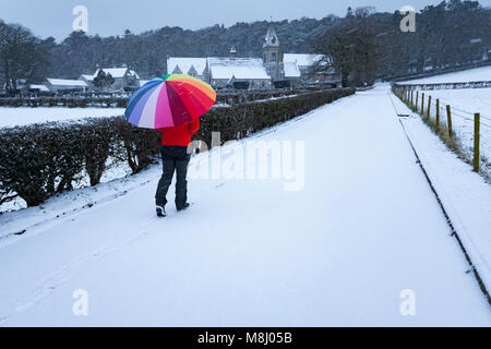 Flintshire, Wales, UK  With Met Office Warnings in place for snow the Mini Beast from the East brings a chill to Flintshire with freezing temperatures and snowy conditions with more on the way throughout the next 24hrs. A person walking down a snow covered lane with a mulitcoloured umbrella for protection from the heavy snow fall at the Pantasaph Franciscan Friary, Flintshire Stock Photo