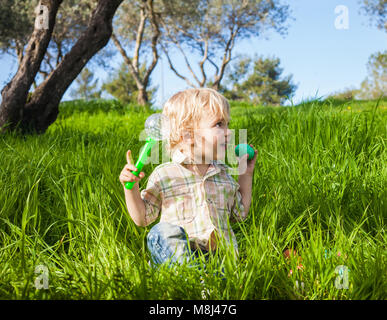 Funny toddler boy pretends to bite a colored Easter egg in the green grass Stock Photo