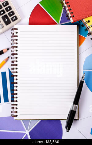 Blank lined paper notebook with ballpoint pen surrounded by various charts and graphs, pencils, books and calculator.  Space for copy. Stock Photo