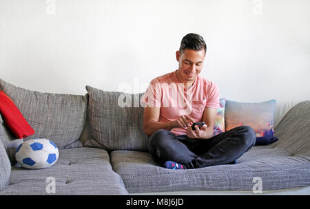 Smiling young man using smartphone on couch Stock Photo