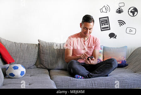 Smiling young man using smartphone on couch Stock Photo