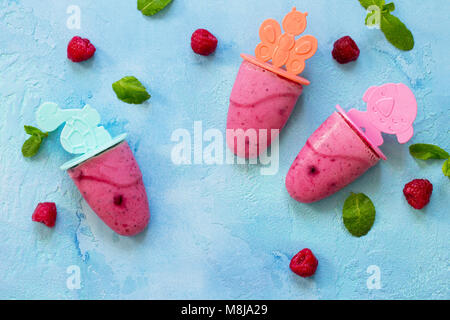 Refreshing children's ice cream popsicles (rasberry sorbet) on blue concrete background. Copy space, top view flat lay background. Stock Photo