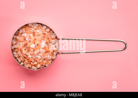 coarse crystals of pink  Himalayan salt in a metal measuring scoop against a pink background, top view Stock Photo