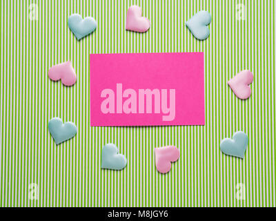 Green striped paper flat lay background with pink card and pastel hearts. Valentine's day message Stock Photo