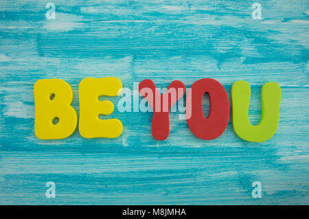 Be You in capital letters on blue colour wash wood background Stock Photo