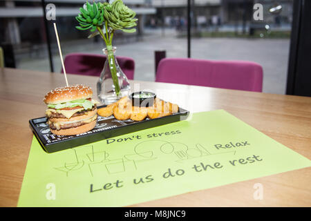 Fast food dish. Appetizing meat burgers, potato chips and vegetable. Takeaway composition. French fries, hamburger and sauces on wooden board with cop Stock Photo