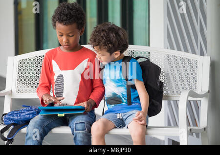 Two boy kid sitting on bench and playing game on tablet at preschoo,Kindergarten school education concept.diversity children Stock Photo