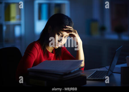 Tired businesswoman working on a laptop at her office desk late in the evening Stock Photo