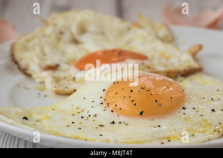 Fried eggs with shells and cracked black pepper, close up. Shot on white driftwood. Stock Photo