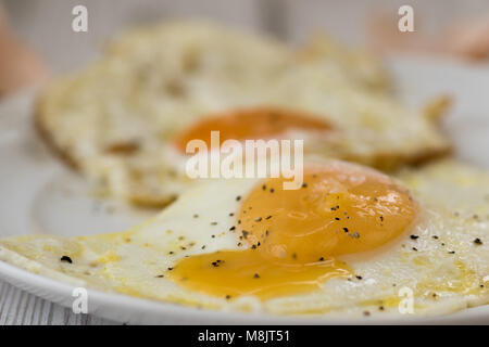 Fried eggs with shells and cracked black pepper, close up. Shot on white driftwood. Stock Photo