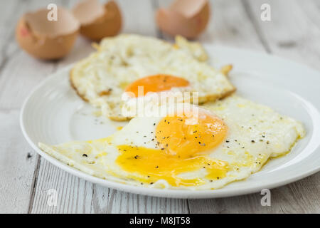 Fried eggs with shells and cracked black pepper, close up. Shot on white driftwood. Stock Photo