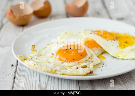 Fried eggs with shells and cracked black pepper, close up. Shot on white driftwood. Stock Photo