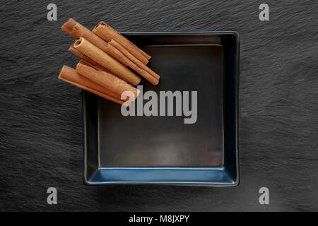Pile dried cinnamon sticks placed on black plate which placed on black stone surface background Stock Photo