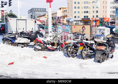 Hunchun, Jilin, China - 8 March 2018: Mopeds and motor scooters and motobikes and motorcycles are many in the snow on the street of the northern provi Stock Photo