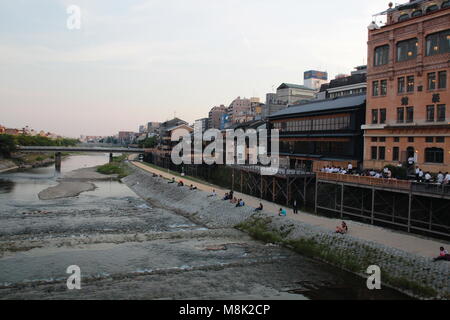 People are relaxing at the Kamo river riverbank in the central of Kyoto, Japan at dusk. Stock Photo