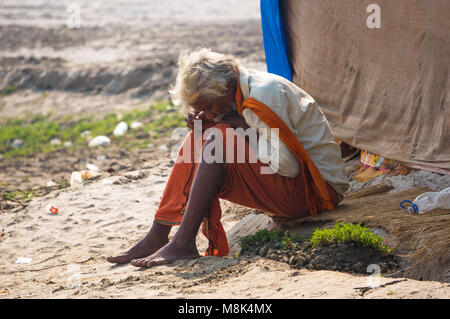 VARANASI, INDIA. February 28, 2017: The hermit, a sadhu, sits meditating on the opposite of the Varanasi banks of the Holy river Ganges Stock Photo