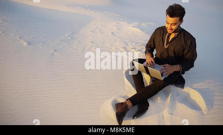 Handsome young Arab man writes on Internet using laptop and sits Stock Photo