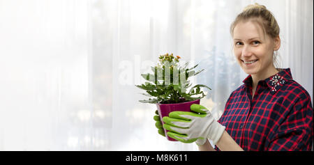 young smiling woman holding flowerpot in hands indoors. copy space Stock Photo