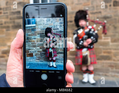Tourist taking photo of Scottish man in tartan playing bagpipes on the Royal Mile in Edinburgh Old Town, Scotland, United Kingdom Stock Photo