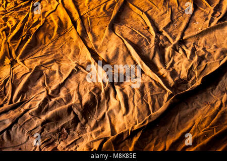 Crumpled old textile material on the ground illuminated with natural warm light. Stock Photo