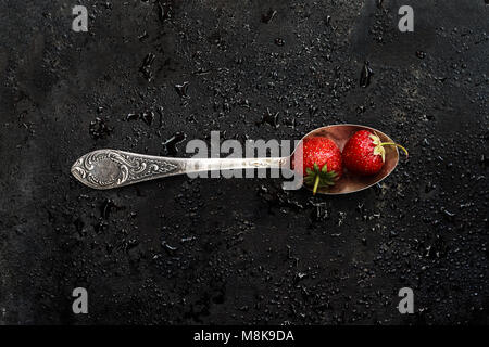 in a spoon a wet strawberry on a dark background with splashes of water, top view. Stock Photo