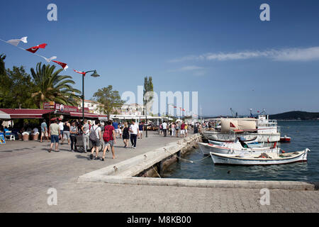 Many people walk by Aegean sea in old town of Cunda (Alibey) Island. Sunny summer day. Stock Photo