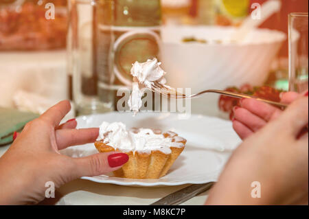 A woman holds a cupcake with white egg white cream, sitting in a cafe. Stock Photo