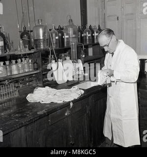 1950s, historical, adult male research scientist in a chemical laboratory analysing samples of linen cloth. Stock Photo