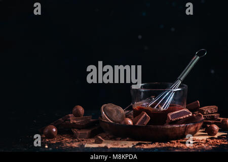 Melted chocolate glazing in a glass cup with a whisk. Dark chocolate and milk chocolate chunks with cinnamon and other spices on a black background. Stock Photo
