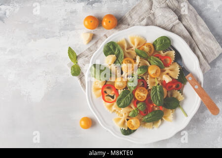Italian pasta farfalle salad with vegetables, basil and spinach in a white plate. Light background Stock Photo