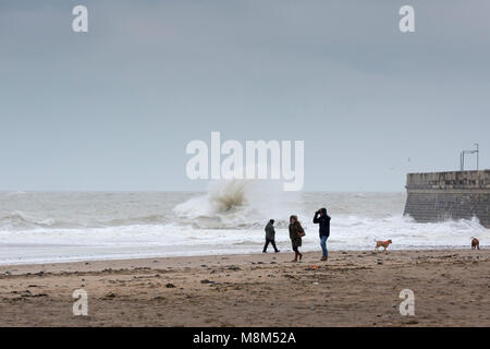 Ramsgate beach, Kent, UK. 3 people and 2 dogs walk on Ramsgate beach in a storm with a large wave behind, 18th March, 2018. Sue Holnes Credit: Sue Holness/Alamy Live News Stock Photo