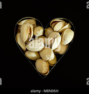 aw pistachios in shell in heart cookie cutter close-up against black background- healthy food concept Stock Photo